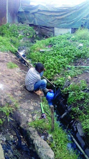 Water pipes: Water pipes criss-cross the slum but not to homes. Here a boy gets water from a leak, his container partly in the litter and contaminated water in the drain.