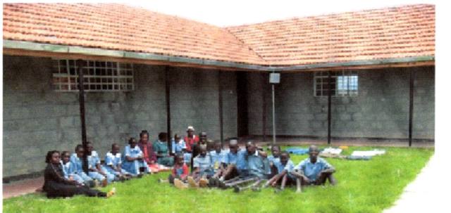 Children seated on the grass in front of the Gilgil Township hostel building.
