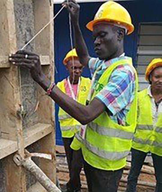 A trainee in a yellow hard hat setting form work for a concrete pour.