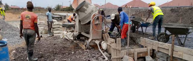 Builders mixing cement on site with houses of the neighbouring estate behind.