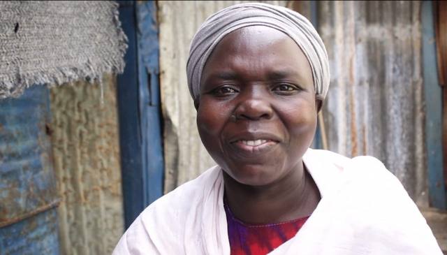 Mary, a member of MWAMKO, smiling in a white top in front of her home.