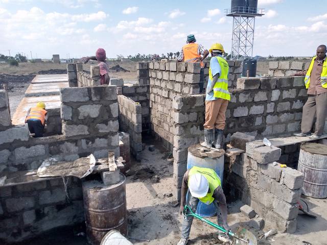 Builders raising block walls at Kamulu with the water tower rising behind them.