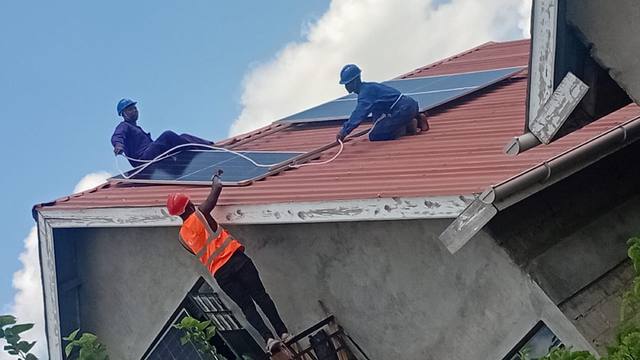A worker fitting a solar panel on a red roof at the Kamulu project.