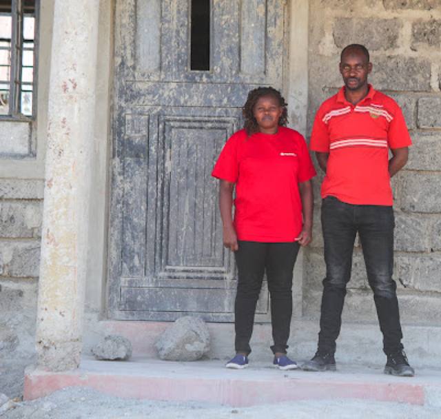 Two MWAMKO residents in red tops standing outside their new front door.